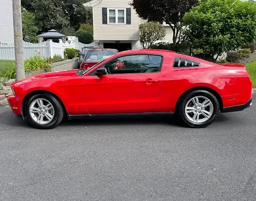 Side view of a bright red Mustang parked on asphalt in front of a suburban home.