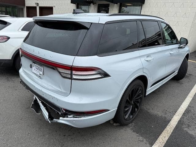 A light gray Lincoln Aviator SUV parked with significant damage to its rear bumper and passenger-side quarter panel.