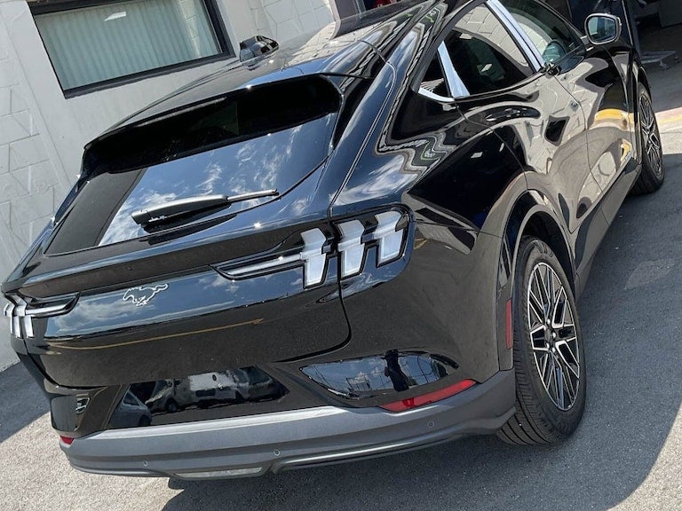 Rear three-quarter view of a shiny black Ford Mustang Mach-E SUV, featuring the iconic Mustang emblem.