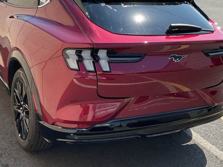 Rear view of a shiny burgundy Ford Mustang Mach-E with its iconic pony emblem and distinctive taillights.