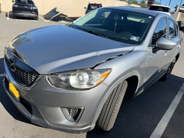 Front-three-quarter view of a gray Mazda CX-5 with damage to its hood and front fender on the driver's side.