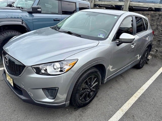 A silver SUV, model Mazda CX-5, parked on asphalt, with a blue Ford Bronco behind it.