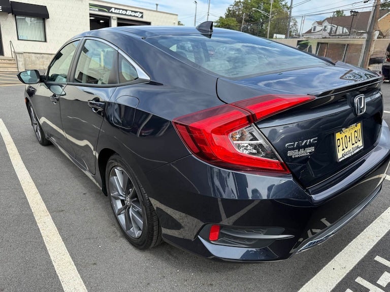 Rear passenger side view of a dark blue Honda Civic sedan parked in a lot, with a building in the background.